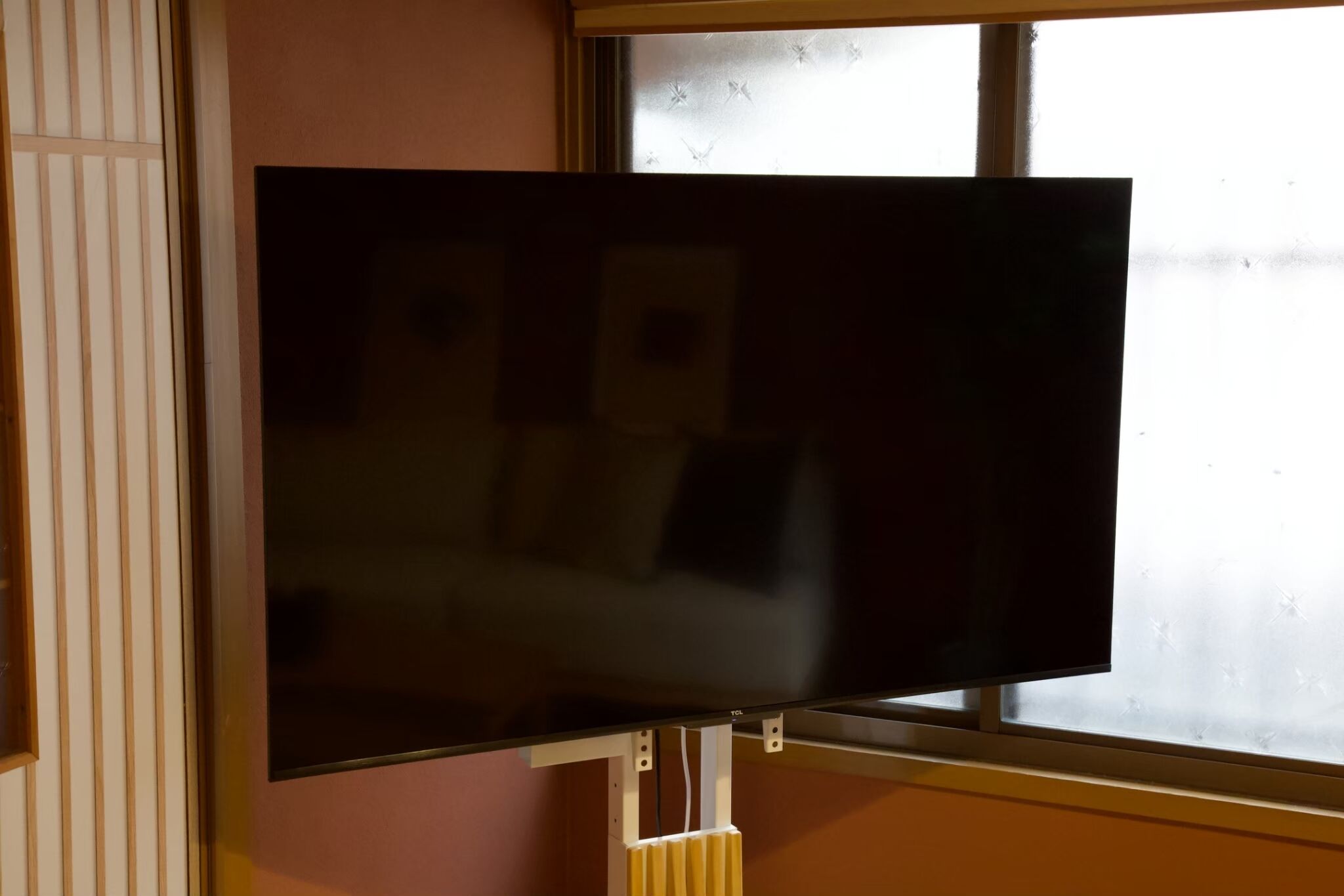 Un televisor montado en una pared con una ventana al fondo.