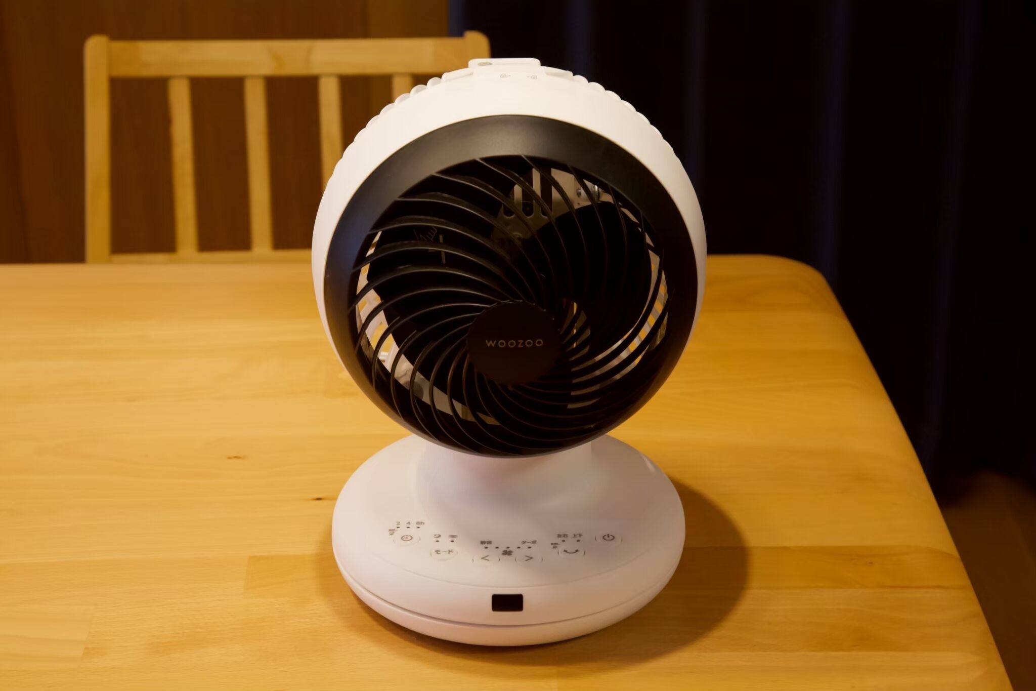 Un ventilador eléctrico blanco con rejilla negra y panel de control sobre una mesa de madera.