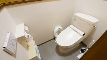A small, compact bathroom with a toilet, a hand dryer, and a paper towel dispenser.