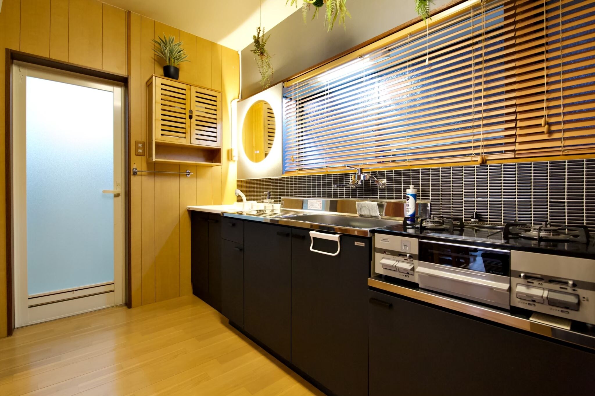 A modern kitchen with a wooden door, built-in cabinets, a stove, and a window with blinds.