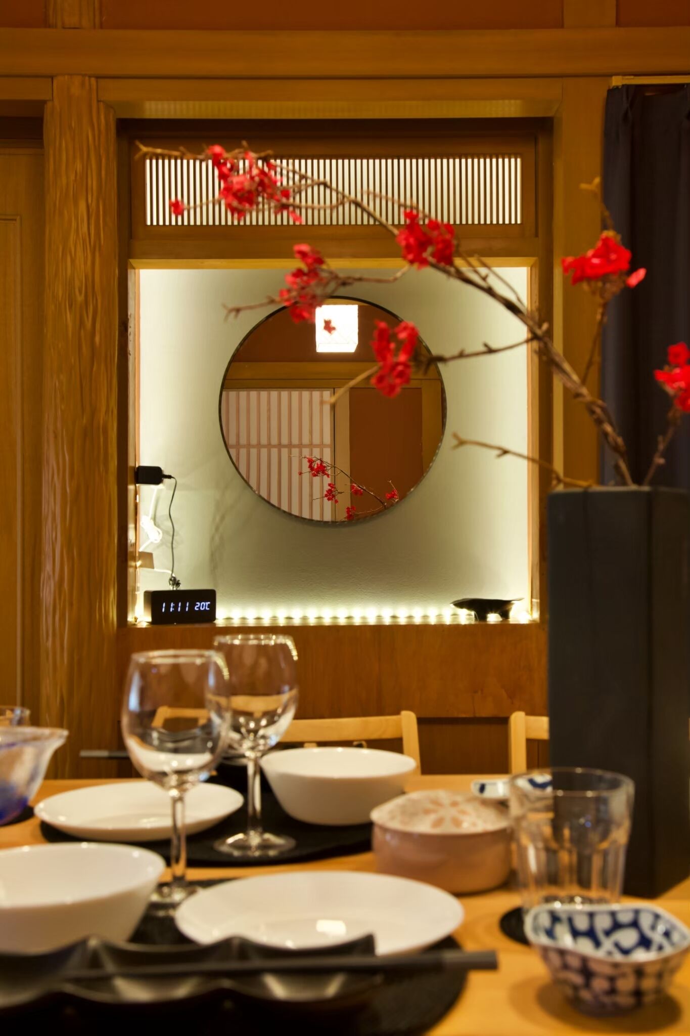 A dining table set with plates, glasses, and a vase with red flowers.