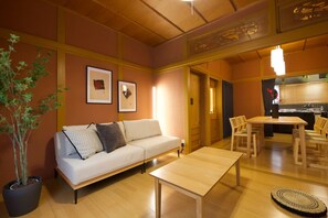 A living room with a sofa, a coffee table, a dining table with chairs, a potted plant, and framed pictures on the wall. - B-STAY TAKAMATSU Gold Ship (Takamatsu)