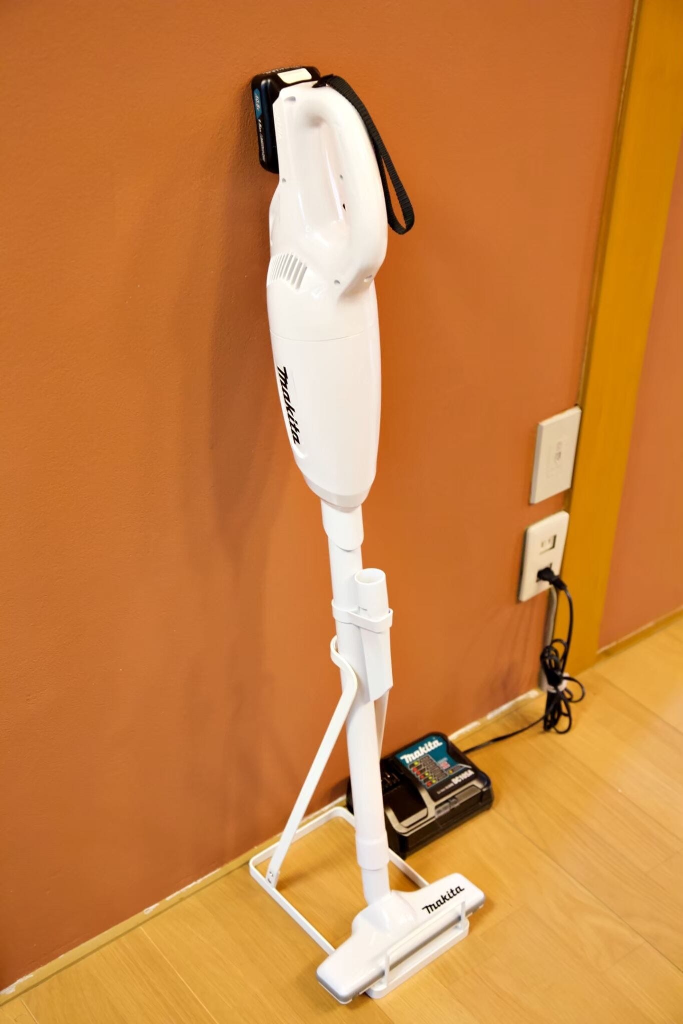 A white vacuum cleaner standing on a wooden floor against a wall.