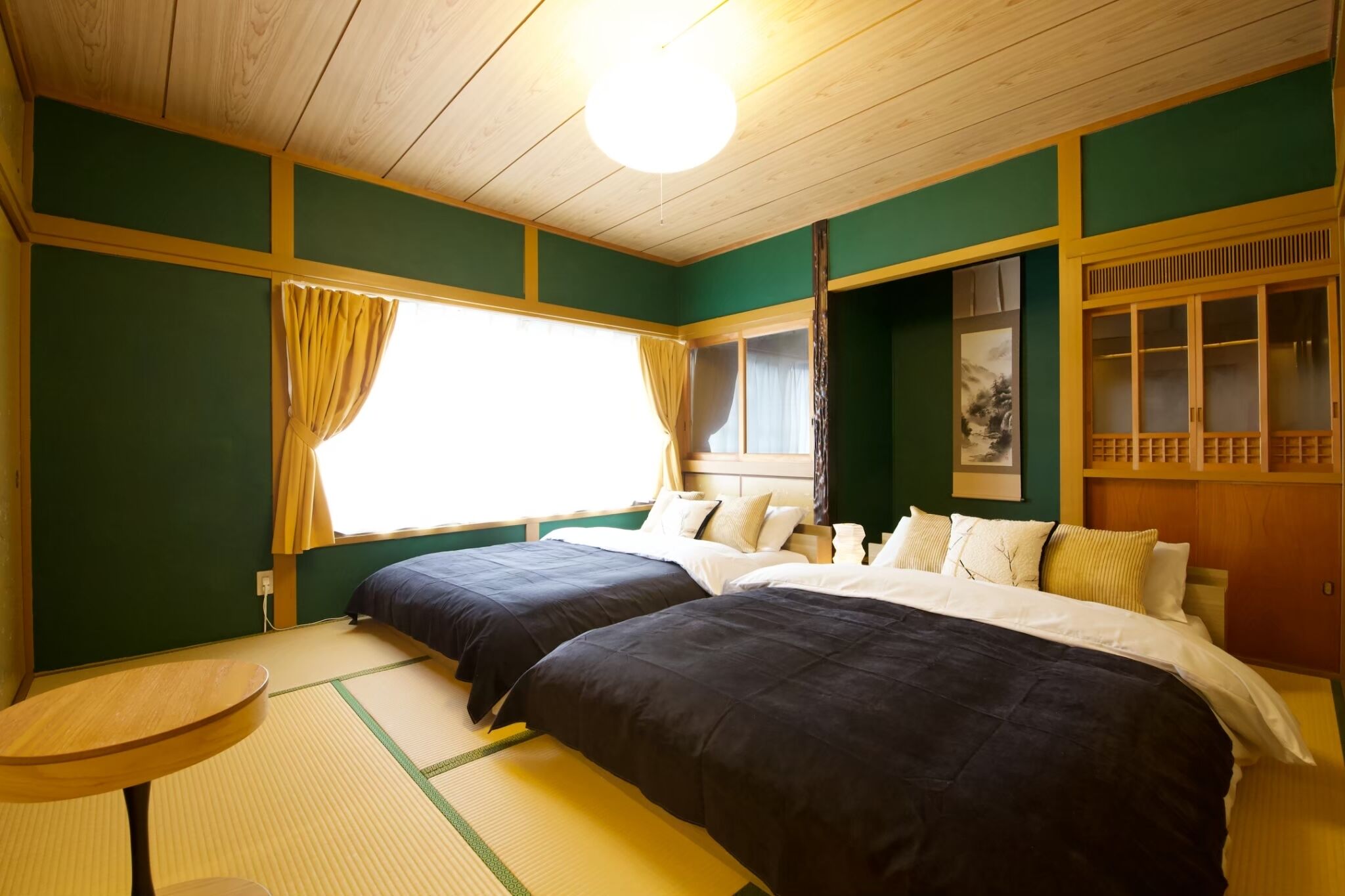A room with two beds, a small table, tatami flooring, a window with curtains, and a traditional wooden cabinet.