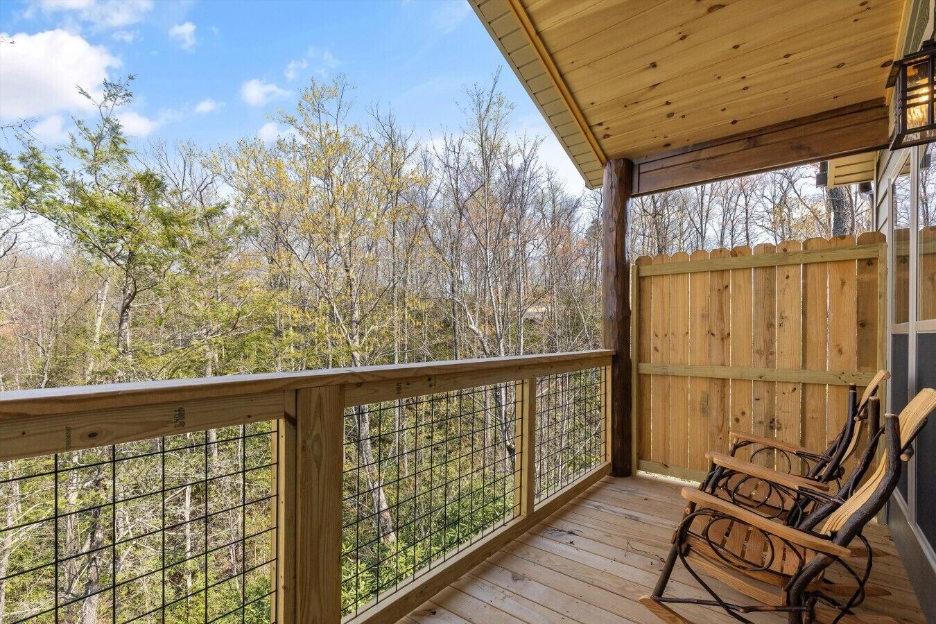 A wooden deck with a railing, a rocking chair, and a view of trees.