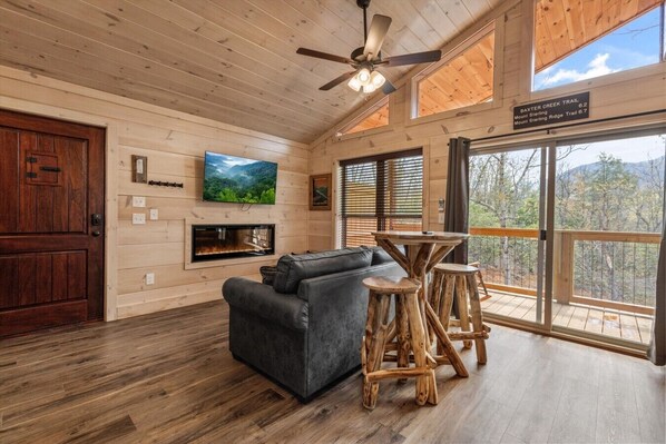 Ein Holzinterieur mit Kamin, einer Couch, einem Fernseher und einem Balkon mit Blick.