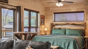 Une pièce de cabane en bois comprenant un lit, une chaise, une table et une fenêtre avec des stores.