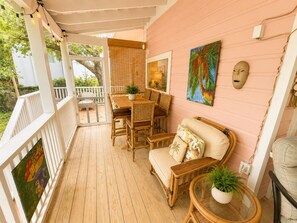 Eine überdachte Veranda mit Holzboden, Korbmöbeln und einer rosafarbenen Wand.