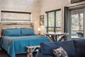 Una habitación tipo cabaña de madera con una cama, una mesa y un ventanal.