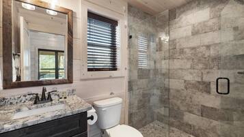 Une salle de bain avec un lavabo en marbre, des toilettes, une douche à parois de verre et un grand miroir.