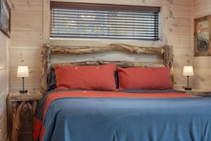 Camera in stile baita con un letto, due lampade da comodino e una finestra con persiane.