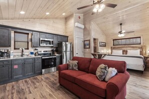 Interior acogedor de una cabaña con kitchenette, un sofá rojo y una cama con cabecera de madera.