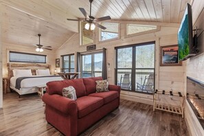 Ein Urlaubsdomizil mit Bett, rotem Sofa, Deckenventilatoren, großen Fenstern und einem Fernseher.