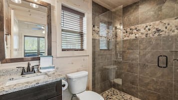 A bathroom with a granite countertop, a toilet, a shower with stone tiles, and a large mirror.