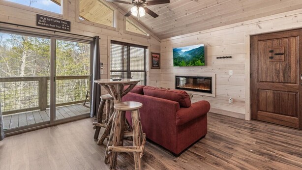 A wooden interior with a sofa, a TV, a fireplace, and a sign indicating Old Settlers Trail. - Gatlinburg 24 min | HotTub +King Bed #8 (Cosby)