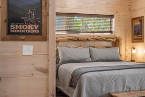 Una habitación tipo cabaña de madera con una cama, un cartel de las Montañas Humeantes y una ventana con persianas.