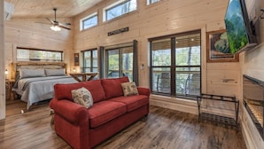 L'intérieur d'une cabane comprend un lit, un canapé rouge, un plancher en bois, des ventilateurs de plafond et un téléviseur fixé au mur.