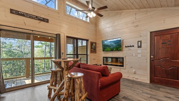 L’intérieur d’un chalet avec un canapé rouge, des tables en bois, une cheminée et un téléviseur fixé au mur.