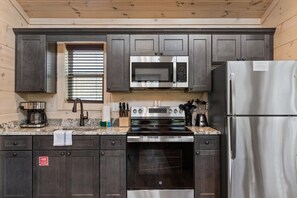 A kitchen with dark cabinets, a stainless steel refrigerator, a microwave, an oven, and a coffee maker. - Gatlinburg 24 min + HotTub +King Bed #5 (Cosby)