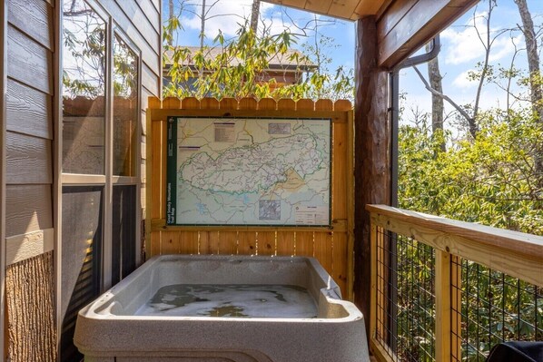 A wooden deck with a map of the Great Smoky Mountains Trail, a stone hot tub, and a view of trees and sky. - Gatlinburg 24 min + HotTub +King Bed #5 (Cosby)