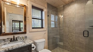 Une salle de bain avec un lavabo en marbre, des toilettes, une douche en verre et un miroir avec un cadre en bois.