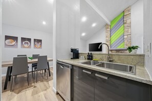 Cocina moderna con lavavajillas, pileta y encimera de granito. Hay un comedor con sillas y una mesa.