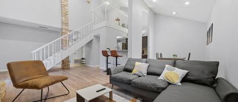 A spacious living area with a high ceiling, a staircase, a sofa set, and a coffee table.