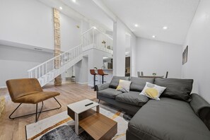 Ein großzügiger Wohnbereich mit hoher Decke, einer Treppe, einer Sofagarnitur und einem Couchtisch.