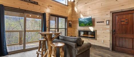 Ein Blockhauskamin mit Holzvertäfelung, einem Kamin, einem Fernseher und Blick ins Freie.