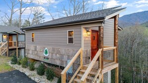 Una baita con veranda in legno, una scala e vista sulla foresta circostante.