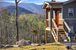 Eine Holzhütte mit einer Holztreppe, die zu einer Terrasse führt, umgeben von Wald und Bergen.