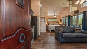 Interior de uma cabana de madeira com uma mesa de jantar, um sofá, uma cama e um ventilador de teto.