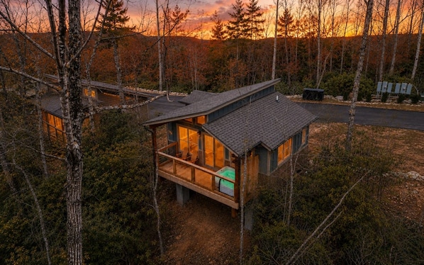 Une cabane dotée d’une terrasse, entourée d’arbres, avec un coucher de soleil en toile de fond.