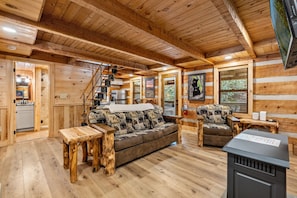 A log cabin interior with a wooden staircase, a sofa with animal print cushions, a dining table, and a fireplace. - Creekside Retreat with 2 Cabins (Gatlinburg)