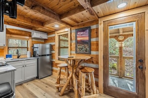 A cabin interior with a kitchen, dining area, and a large window with a view. - Creekside Retreat with 2 Cabins (Gatlinburg)