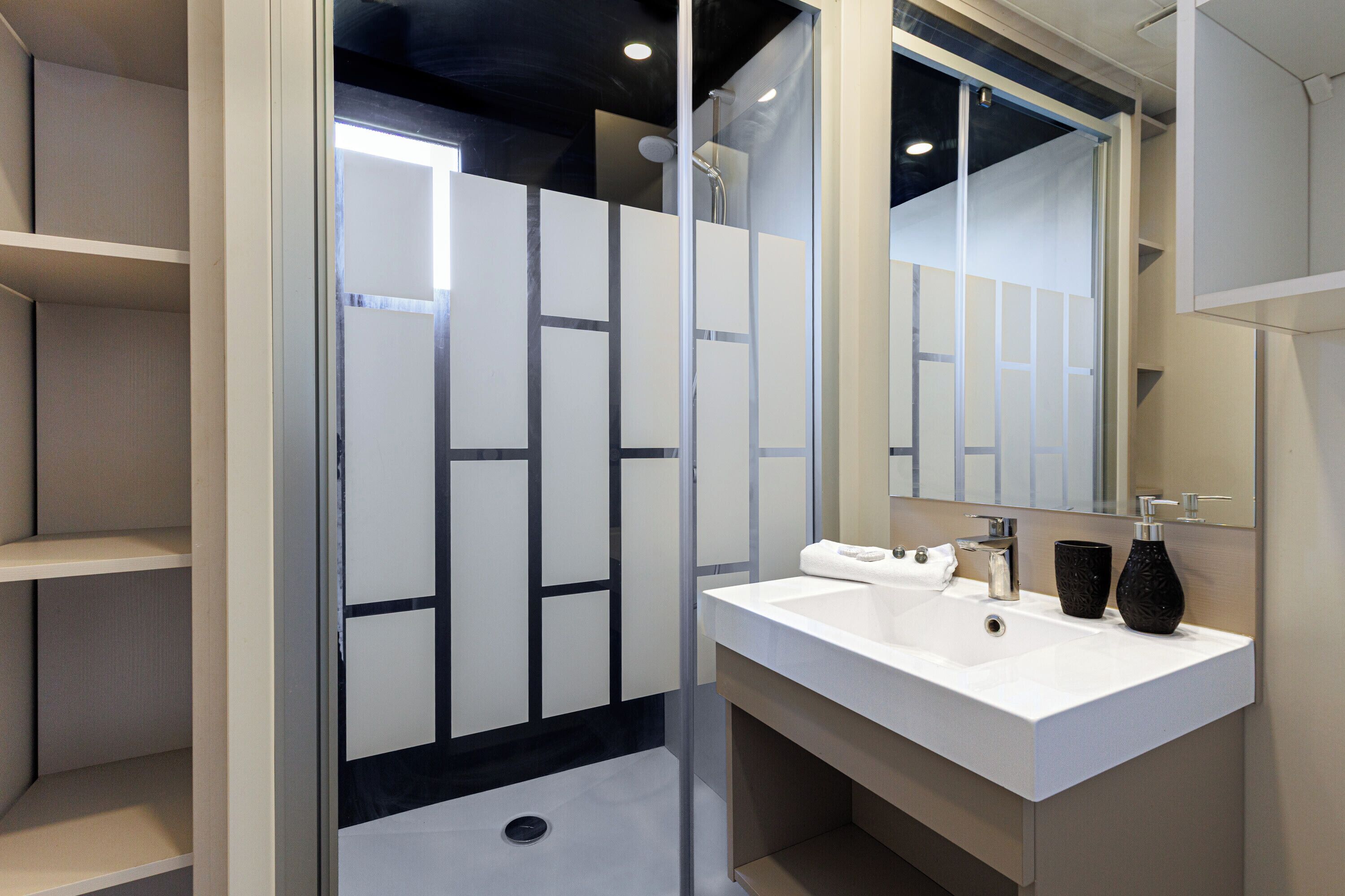 Une salle de bain moderne avec une douche à parois de verre, un lavabo blanc avec un miroir et un vase noir posé sur le plan de travail.