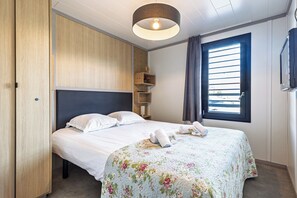 Ein Schlafzimmer mit Bett, Kleiderschrank, Fernseher und einem Fenster mit Jalousien.