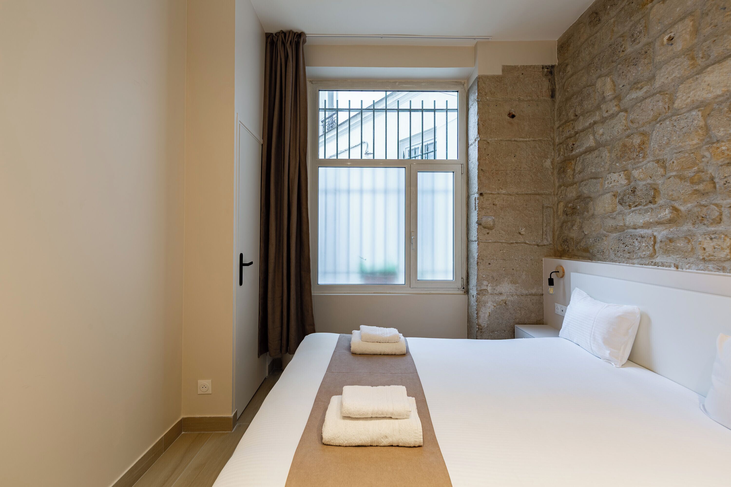 A hotel room with a large bed, a stone wall, and a window with a view.