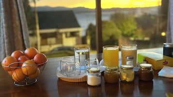 A breakfast setting with oranges, glasses, and condiments on a table with a view of a house and mountains.