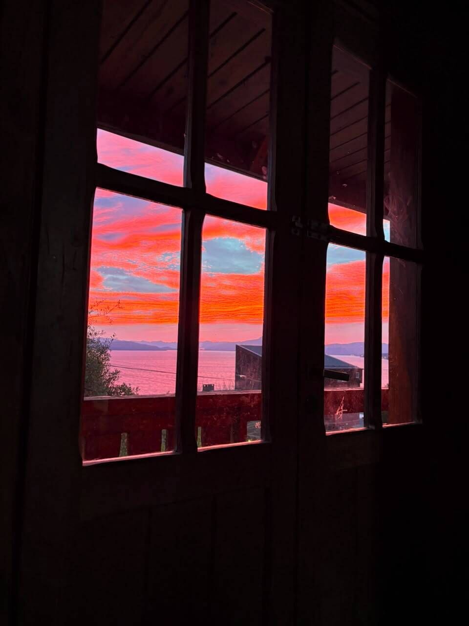 Una finestra amb vista al sol ixent sobre un conjunt d'aigua i muntanyes llunyanes.