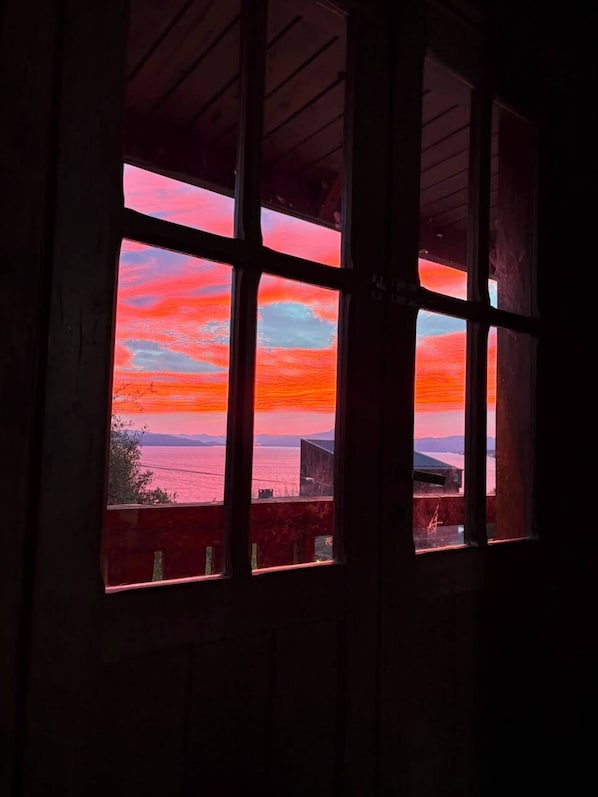Una ventana con vista a una puesta de sol sobre una masa de agua y montañas distantes.