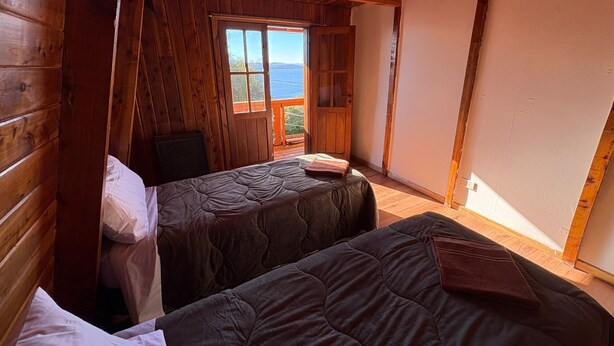 A cabin with two beds, wooden walls, a window with a view, and a ceiling fan.