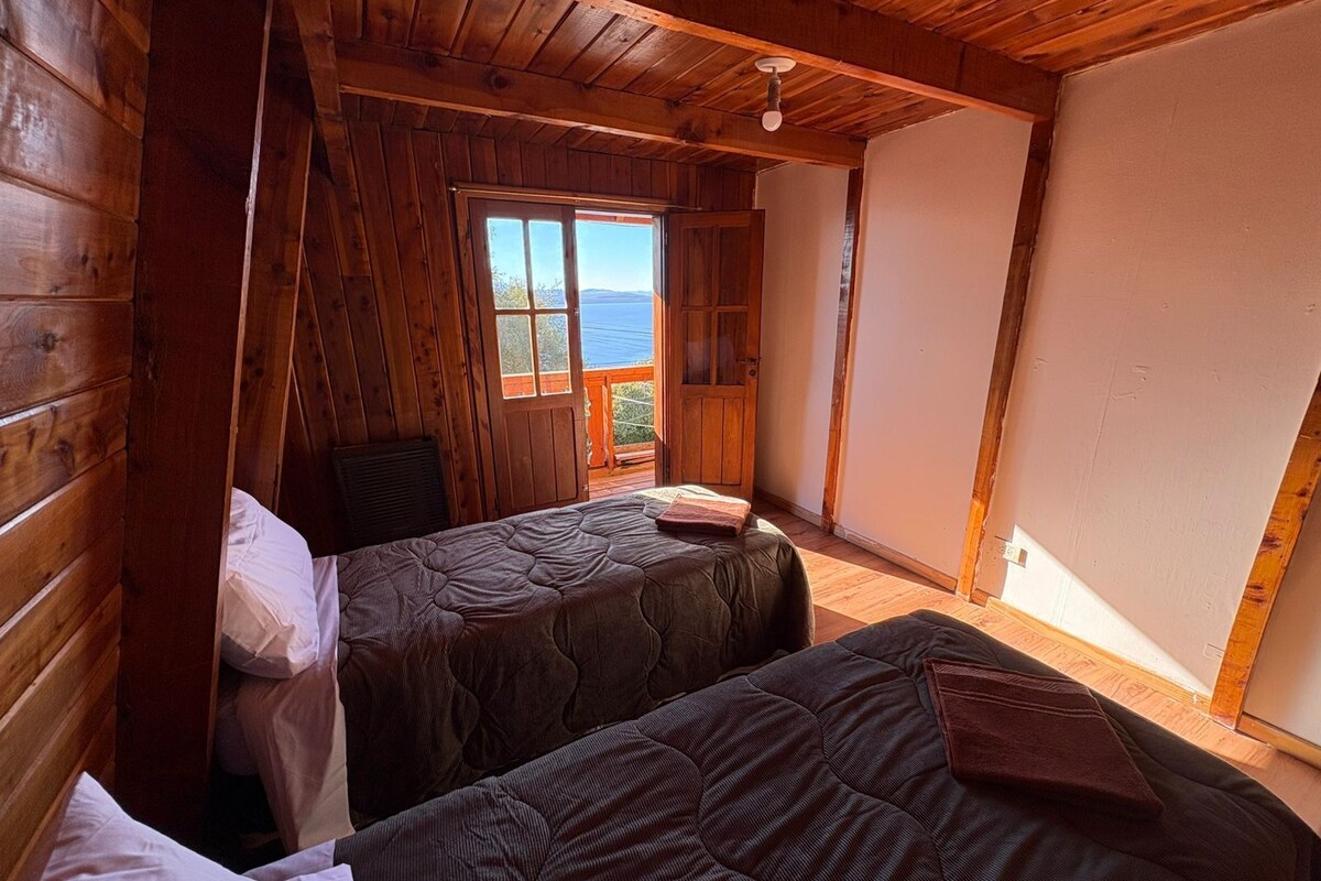 Una cabaña con dos camas, paredes de madera, una ventana con vistas y un ventilador de techo.