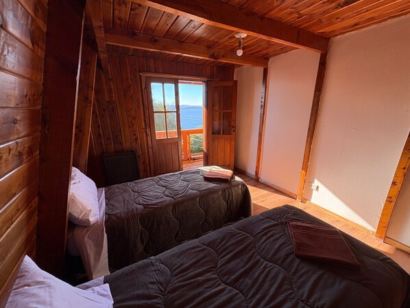 A cabin with two beds, wooden walls, a window with a view, and a ceiling fan.