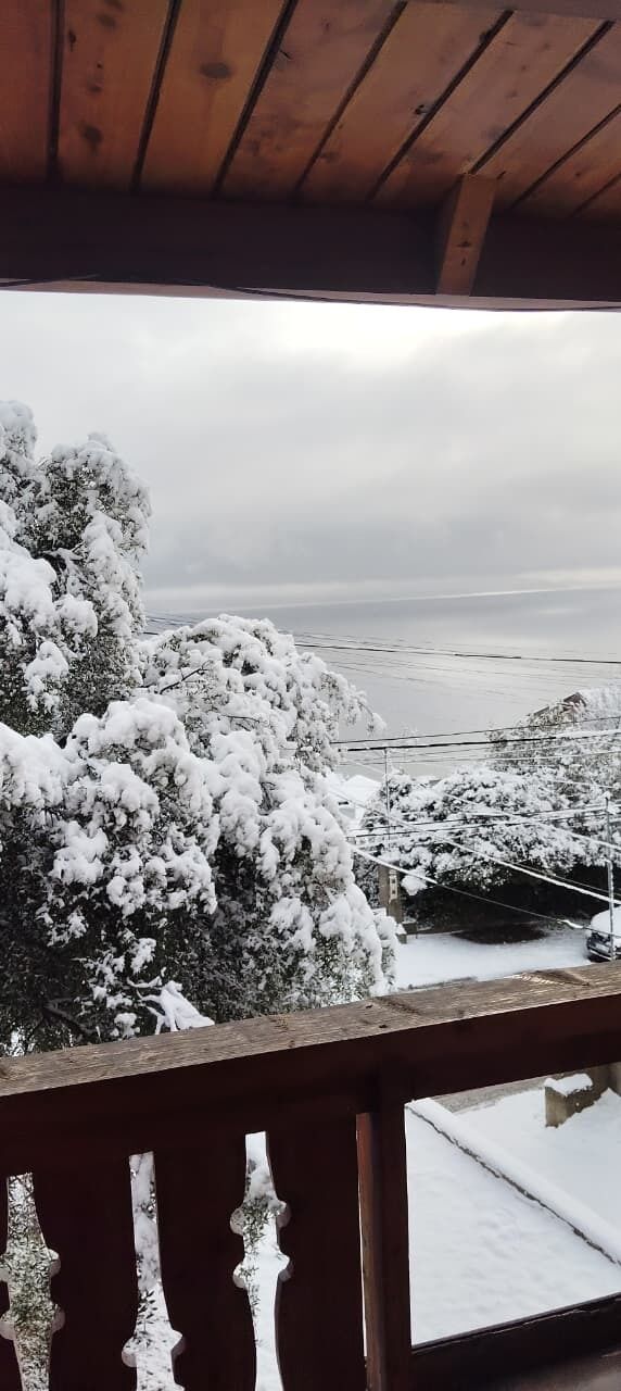A wooden balcony with a view of snow-covered trees and a distant landscape.