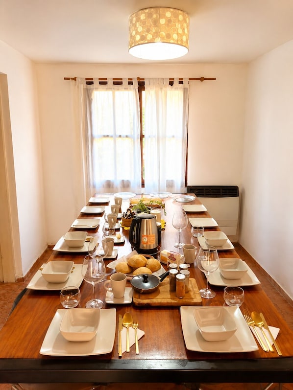 Une longue table à manger, dressée pour un repas, avec des assiettes, des bols, des couverts et une cafetière.