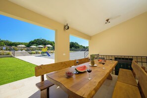 An outdoor dining area with a wooden table, benches, and a view of a playground. - Villa Tone i Maria (Istria - Matohanci) (Matohanci)