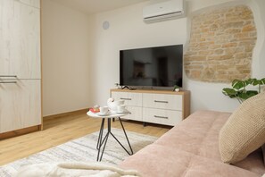 Ein modernes Wohnzimmer mit Flachbildfernseher, einer Wand aus Naturstein, einer Holzeinrichtung und einem gemütlichen Sofa.