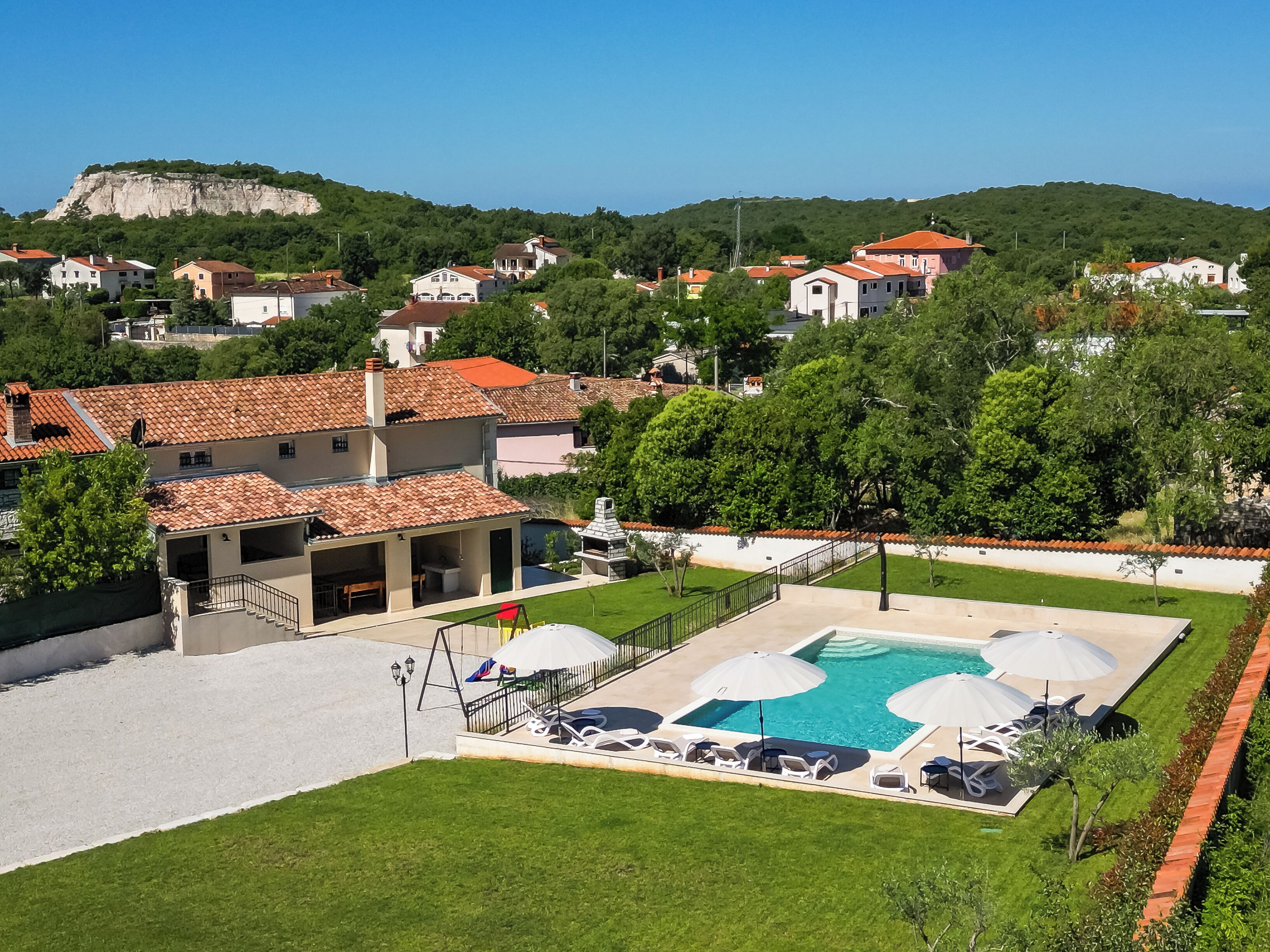 A residential area with a swimming pool, lounge chairs, and a view of a hill.