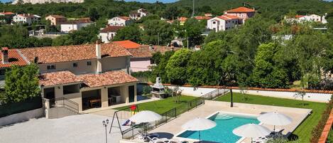 A residential area with a swimming pool, lounge chairs, and a view of a hill.